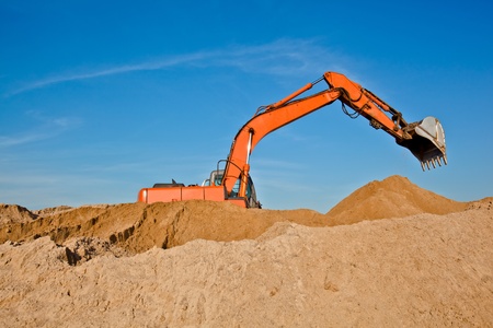 Excavator at sandpit with raised bucket over skyの写真素材