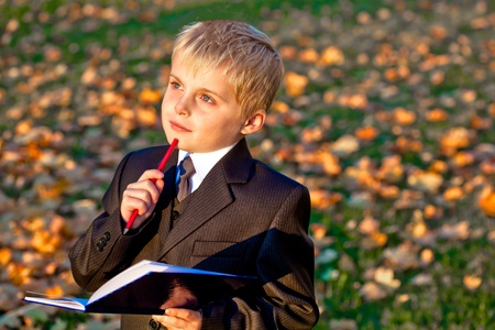 Children little boy pupil with pencil and notebook thinking looking up outdoorsの写真素材