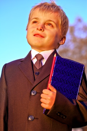 Happy cheerful schoolboy with pencil and notebook on  blue sky backgroundの写真素材