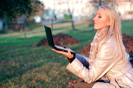 Study time for one young beautiful blonde student girl in autumn park with computer laptopの写真素材