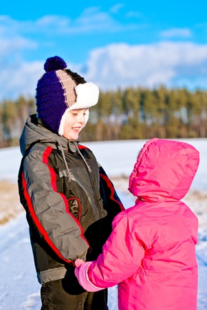 Children boy and girl looking at each other holding hands standing on snow in winterの写真素材