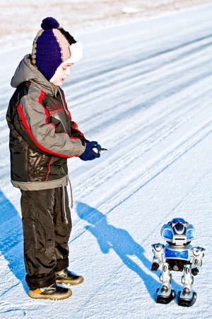 Kid boy playing with toy combat robot on snowの写真素材