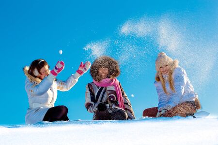 Cheerful girls playing with snow at blue sky backgroundの写真素材