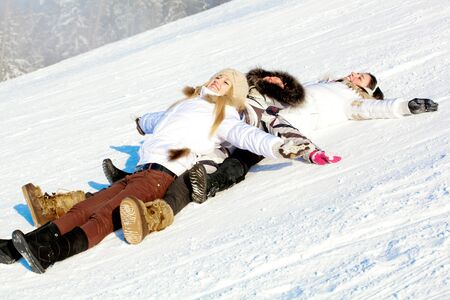 Young positive girls lying down at snow slope in winterの写真素材