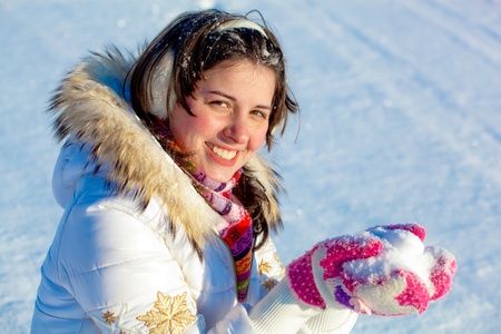 Portrait of cheerful student girl with headphones holding snow in palms outdoorsの写真素材