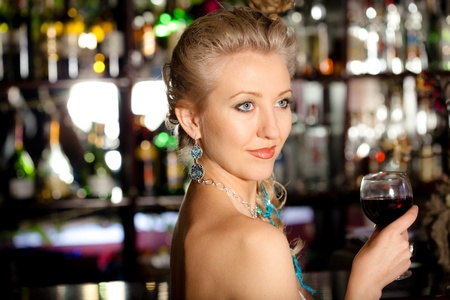 Young beautiful blonde woman with a glass of wine standing at a bar counterの写真素材