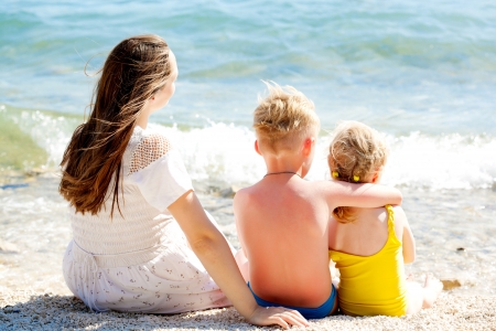 Young mother and her two kids relaxing on the coast of the seaの写真素材