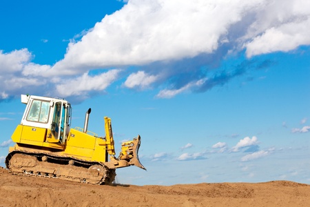 Bulldozer machine moves with raised blade on construction site during earth moving works