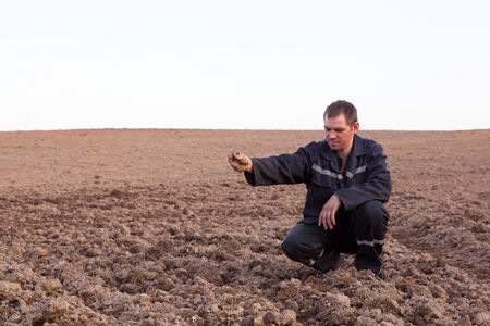 Farmer man in cultivated field looking at soil