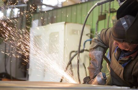 Metalworking industry: factory welder worker grinding steel sheet with flying sparks in workshopの写真素材