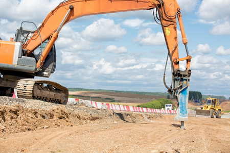 Large jackhammer crushing street asphalt paving during road construction work and wheel loader moving break stones into truck lorryの写真素材