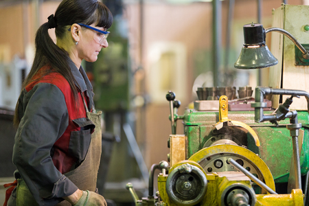 Factory woman turner working at workshop lathe machineの写真素材