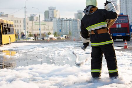 Fireman standing among firefighting foam and carrying fire hose reel after extinguish fire in public...