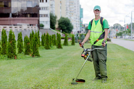 Municipal services senior worker gardener with lawn mover grass trimmer on city street backgroundの写真素材