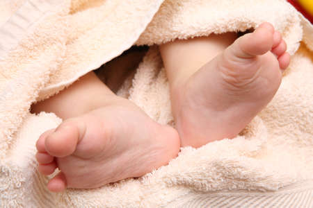 children's feet in the hands of the mother against the backdrop of a pink towelの写真素材