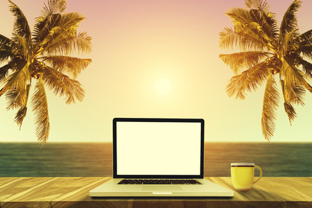 A laptop and a coffee cup on wood table in the sea beach with coconut tree.の写真素材