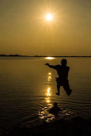 Silhouettes of man who jump off into lake at sunset の写真素材