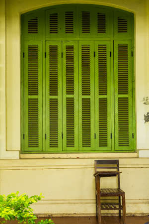 Green vintage wooden windows with student chair, colonial style building from Vientiane, Laos の写真素材