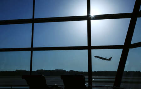 An airplane is taking off behind the airport window