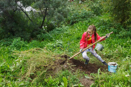 Girl teenager in red jacket digging in green garden