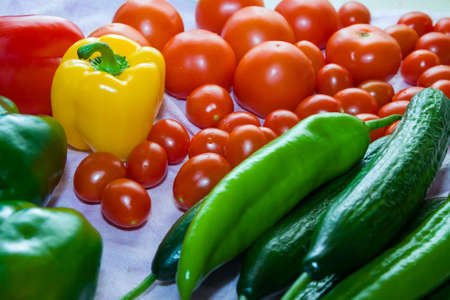 Red tomatoes, yellow and green paprika, cucumbers on a table with drops of waterの写真素材