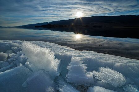 Pieces of melting ice at the shore of Baikal lake at sunset with blue skyの写真素材