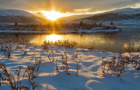 Sunset in mountains after snowstorm with reflection of the sky in lake waterの写真素材