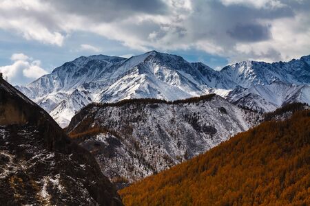 A snowy mountain with yellow forest in front and dramatic clouds