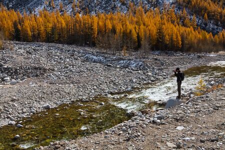 ORLIK, BURYATIYA, RUSSIA - SEPTEMBER 2014: A photographer taking pictures at the rocky bank of mountain river with yellow larch treesのeditorial素材