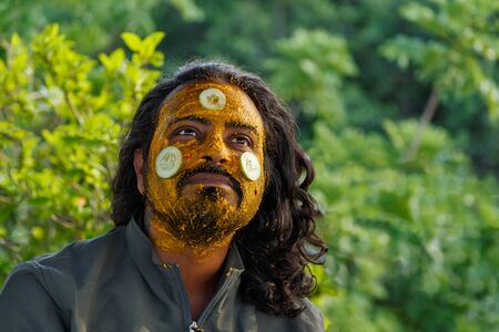 Face portrait of attractive bearded Indian man wearing facial clay mask with turmeric and cucumbersの写真素材