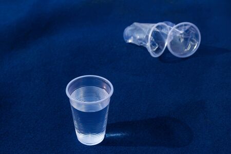 Transparent plastic cup with clear water and two smashed glasses on a blue background withの写真素材
