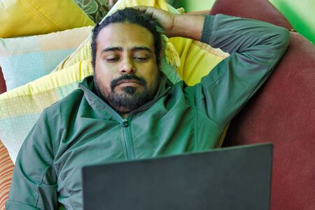 An Indian man lying on sofa and working on his laptopの写真素材