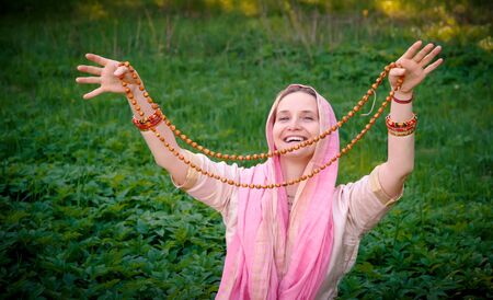 Woman in Indian clothes in a green meadow laughing and showing her meditation malaの写真素材