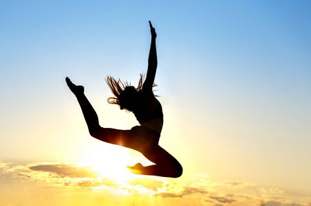 Graceful gymnast dancer jumping leaps against sunsetの写真素材