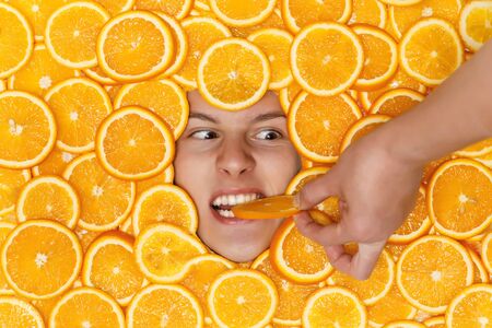 Face of young man on sliced juicy oranges biting a piece from a handの写真素材