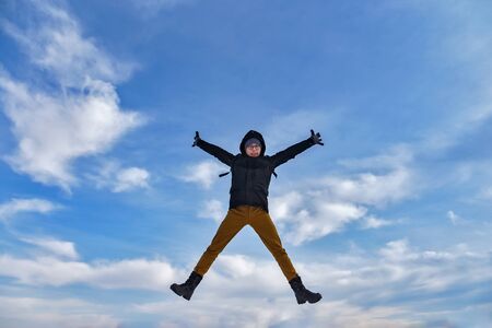 Young man jumping in the air with blue sky in winter with arms and legs to the sidesの写真素材