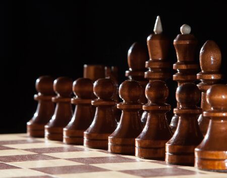 Chess board with black wooden pieces ready for game with dark background
