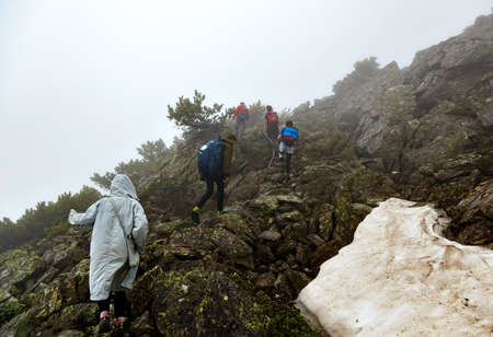 CHAMAR-DABAN, RUSSIA - JUNE 16 2020: Few tourists are hiking up on a rocky path with melting snow in fogのeditorial素材