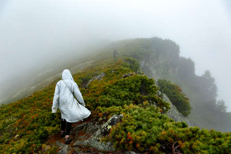 CHAMAR-DABAN, RUSSIA - JUNE 16 2020: Two tourists on a rocky hill covered with cedar bushes in a cloud hiking upのeditorial素材