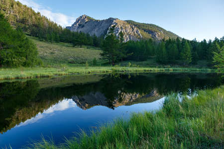 Small mountain lake with reflection of green forest and rocks in the morning