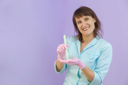 Attractive woman in green uniform and pink gloves smiling with a cup of a facial cream in her hands