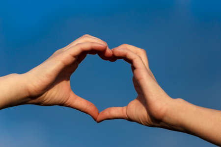 Girl hands in heart form over blue sky backgroundの写真素材