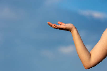 A womans hand against the blue sky with her palm turned upの写真素材