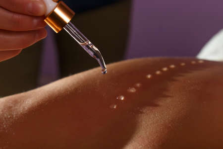 Hand of a masseur applying oil drops on a female backの写真素材