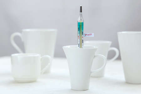 Many white cups on the table, one of them with thermometer with inscription Cosy