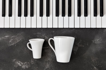 Keyboard of a piano with one small and one bigh white mugs in front of itの写真素材