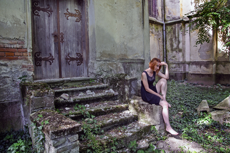 Sad and lonely young girl in red sitting on the old stairs and imagination.の写真素材