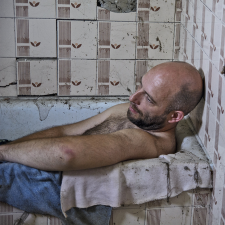 A man sits in an old bathtub and thinks about the past.