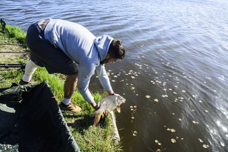 A young fisherman with a newly caught carp poses before catching back into the water.