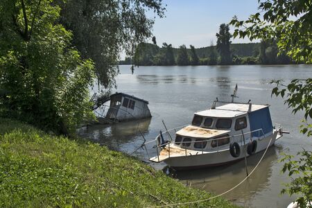 Novi Becej, Tisa River, May 14, 2017. Two yachts moored along the riverbank. One has sunk and is now the only cable holding it to the shore to keep the river from deep.のeditorial素材